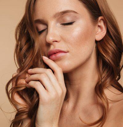 Close up Beauty portrait of sensual ginger woman with long hair posing with closed eyes over cream background